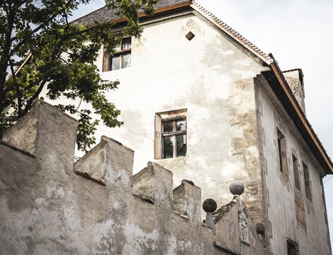Old white building with weathered walls and a tree beside it in Brixen Südtirol.