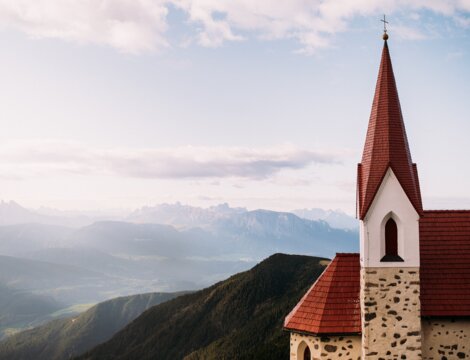 Chiesa con campanile rosso sopra la valle di Brixen Südtirol, con le cime sullo sfondo.