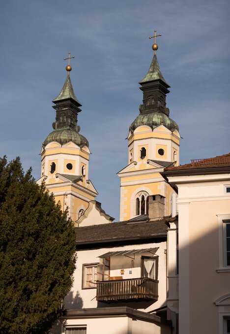 Zwei Kirchtürme mit Zwiebeldächern ragen über historische Gebäude vor blauem Himmel empor.