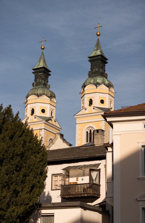 Two church towers with onion domes rise above historic buildings under a clear blue sky.