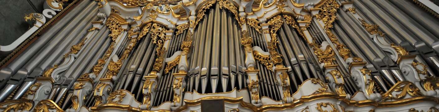 Ornate baroque pipe organ with gold detailing inside a church.