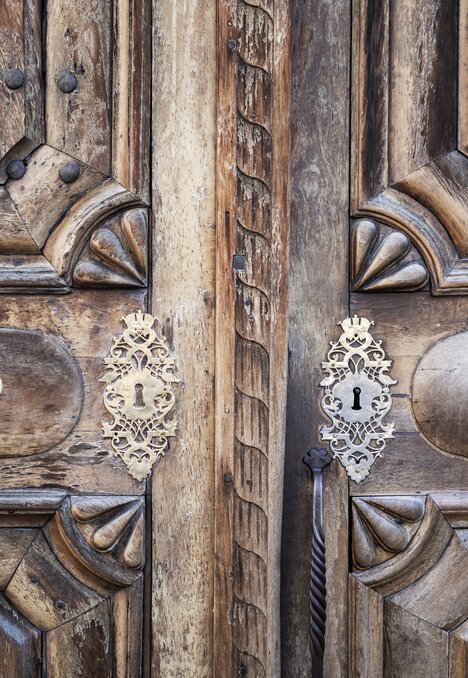 Porta doppia in legno intagliato con decorazioni metalliche e antiche serrature.