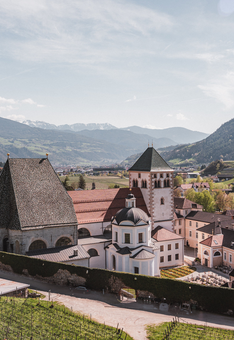 Abbazia storica a Brixen Südtirol con vigneti, borgo in valle e montagne sullo sfondo.