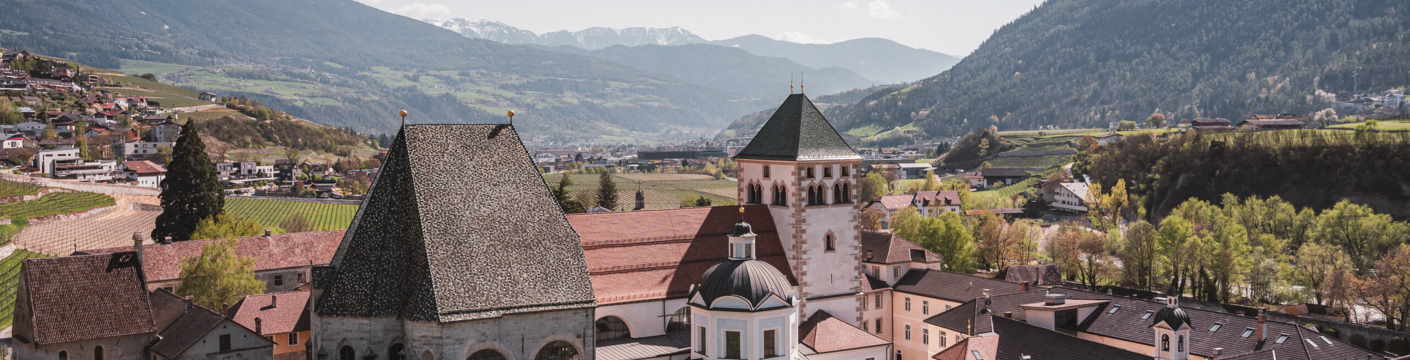 Historisches Kloster in Brixen Südtirol mit Weinbergen, Talort und Bergen im Hintergrund.