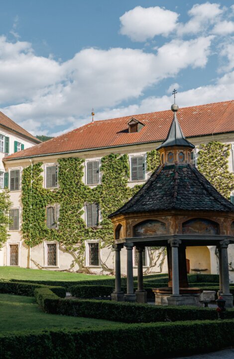 Historischer Innenhof mit efeubewachsenem Gebäude und kleinem Pavillon unter blauem Himmel in Brixen Südtirol.