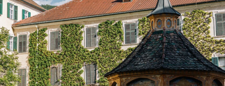 Cortile storico con edificio ricoperto d’edera e piccolo padiglione sotto il cielo azzurro a Brixen Südtirol.