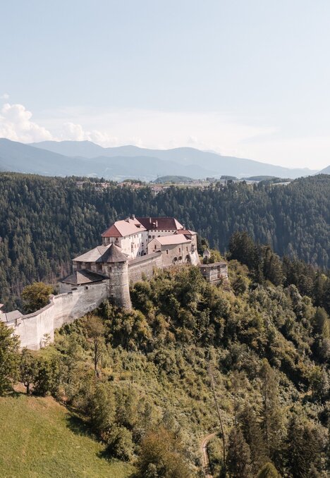 Historische Festung auf einem bewaldeten Hügel über dem Tal in Brixen Südtirol, mit Bergen im Hintergrund.