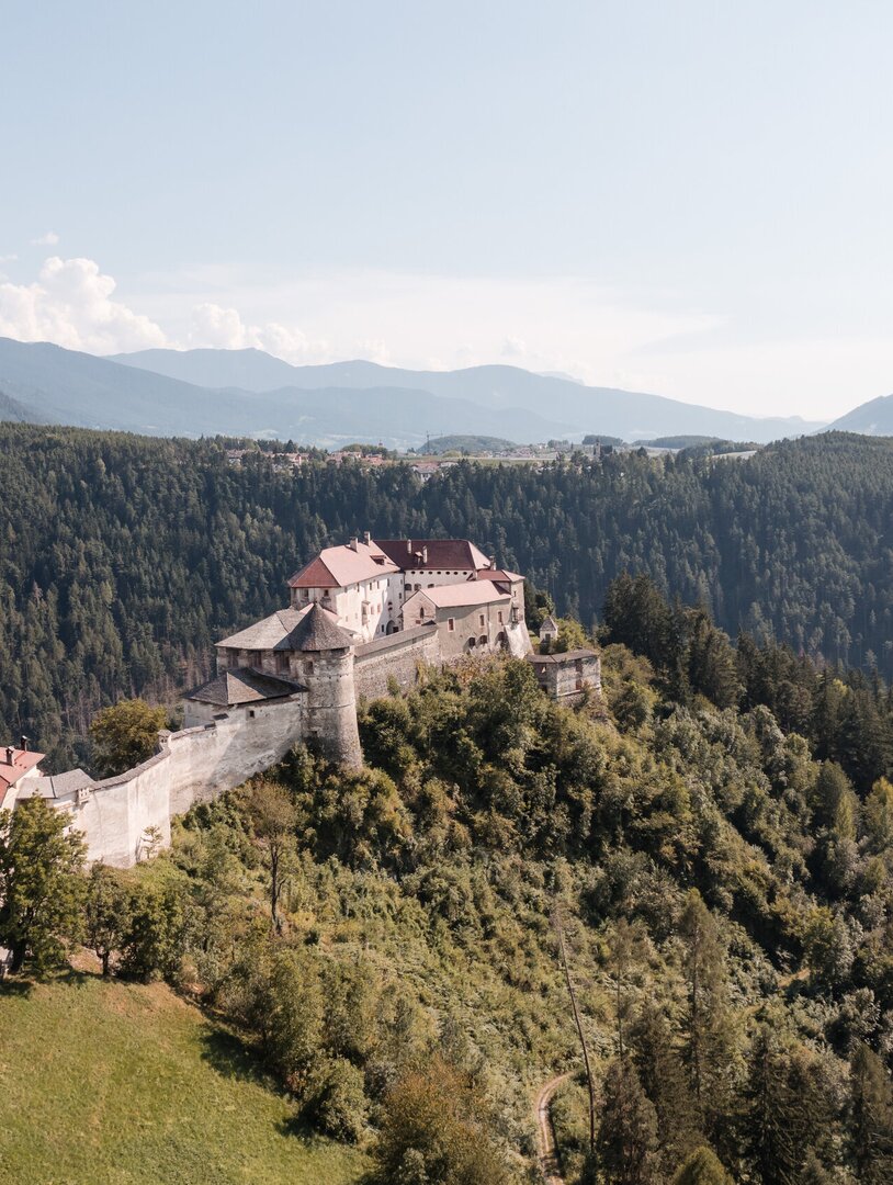 Historische Festung auf einem bewaldeten Hügel über dem Tal in Brixen Südtirol, mit Bergen im Hintergrund.