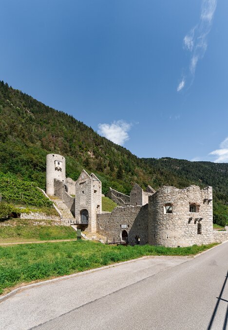 Steinerne Festungsruinen neben einer Straße an einem grünen Hang unter blauem Himmel in Brixen Südtirol.
