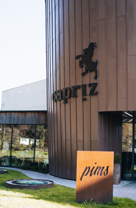 Moderne Außenansicht des capriz-Gebäudes mit Rasen im Vordergrund und orangefarbenem pims-Schild.