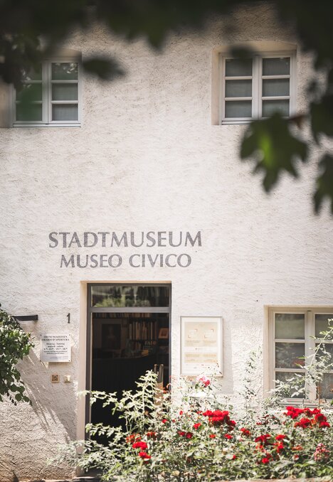 Fassade des Stadtmuseums Museo Civico mit Blumen vor dem Eingang und Blättern im Vordergrund.