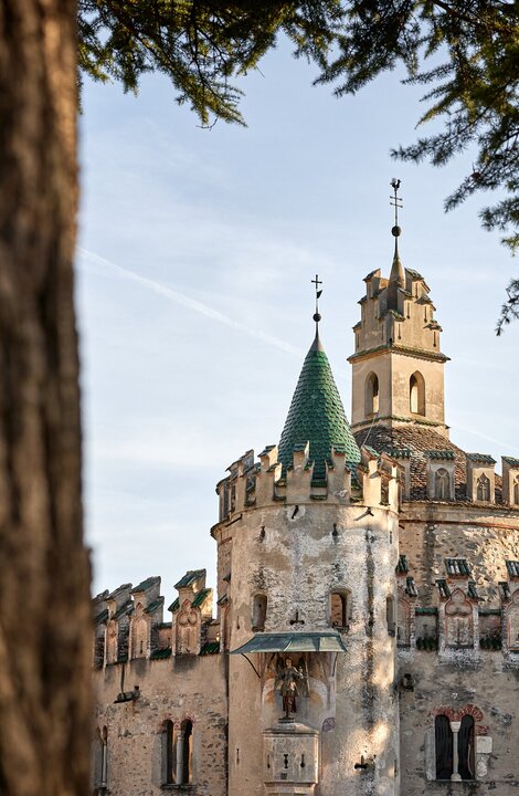 Edificio storico rotondo con torre a Brixen Südtirol, incorniciato da alberi e montagne.