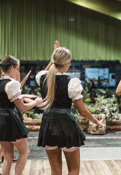 Three women in traditional dress dancing on a stage in a hall.