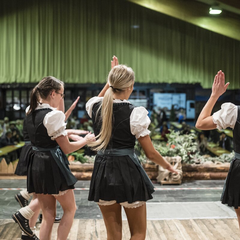 Tre donne in abito tradizionale danzano su un palco in una sala.