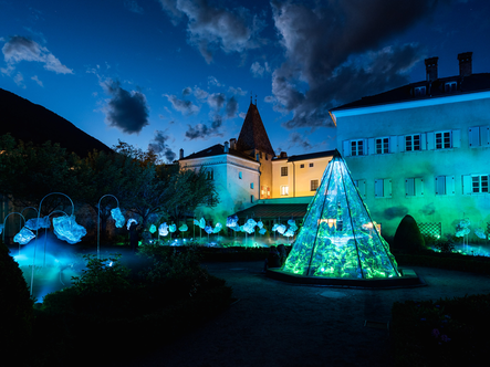 Cortile illuminato con installazione di luce blu e verde accanto a edifici storici di notte.