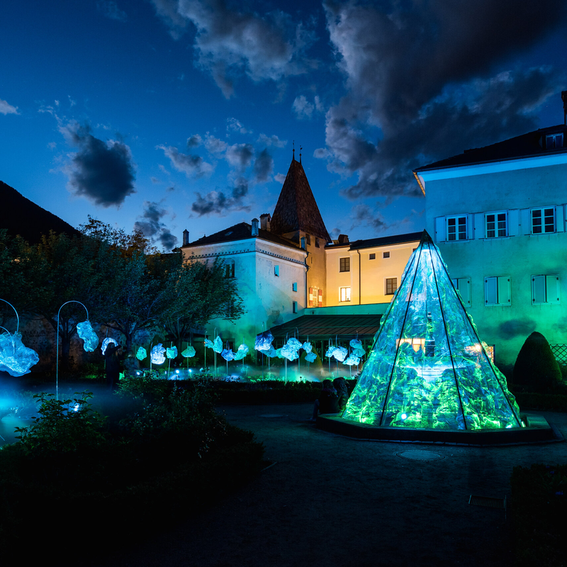 Beleuchteter Innenhof mit blau-grüner Lichtinstallation neben historischen Gebäuden bei Nacht.