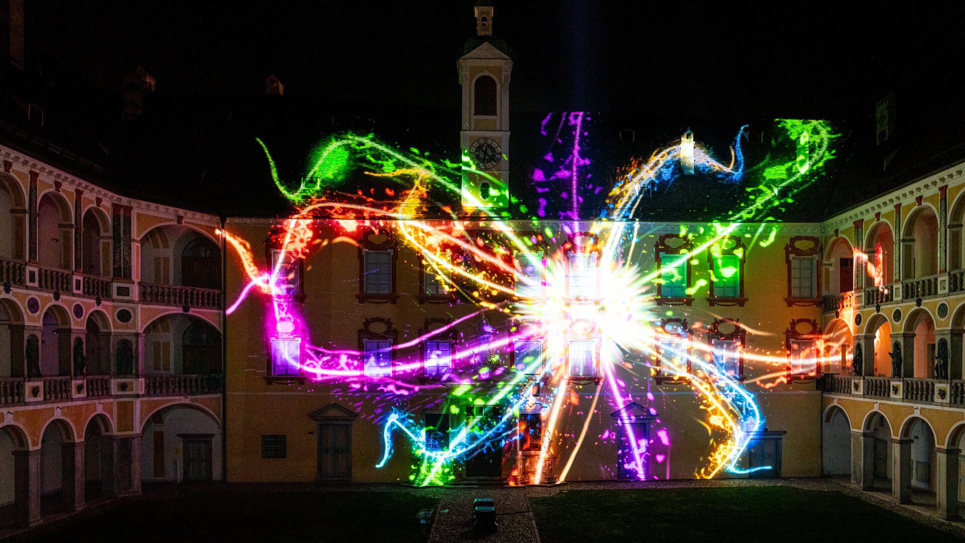 Colorful light projection on historic courtyard buildings at night.