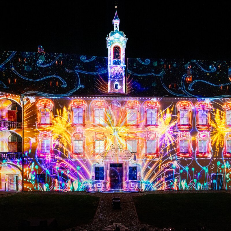 Bunte Lichtprojektionen auf einem historischen Hofgebäude bei Nacht in Brixen Südtirol.