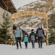 Family walking through snow under a wooden arch at a winter mountain village.
