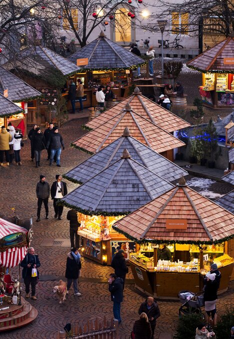 Besucher zwischen beleuchteten Marktständen auf einem Weihnachtsmarkt am Winterabend