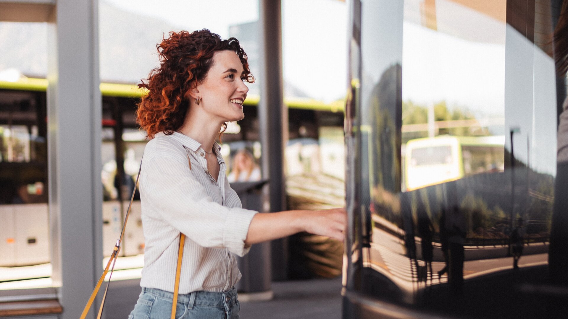 Woman boarding a bus at a modern stop with a yellow shoulder bag.