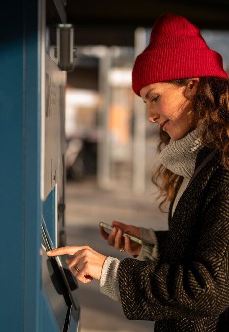 Donna con berretto rosso che usa un distributore di biglietti in stazione | © IDM Südtirol-Alto Adige/Patrick Schwienbacher