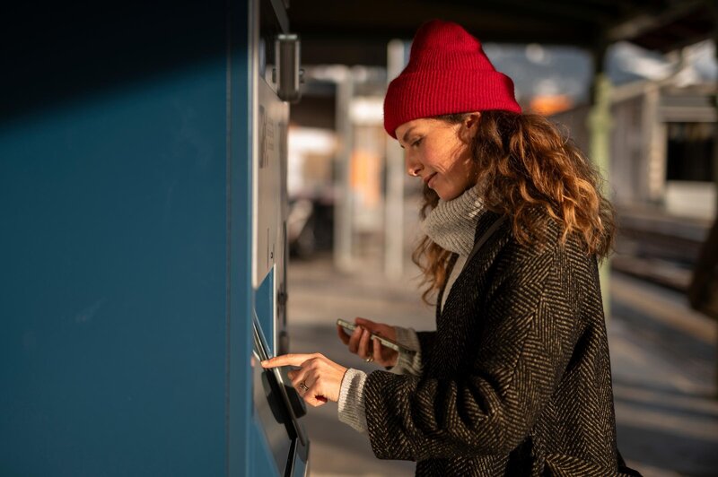 Donna con berretto rosso che usa un distributore di biglietti in stazione | © IDM Südtirol-Alto Adige/Patrick Schwienbacher