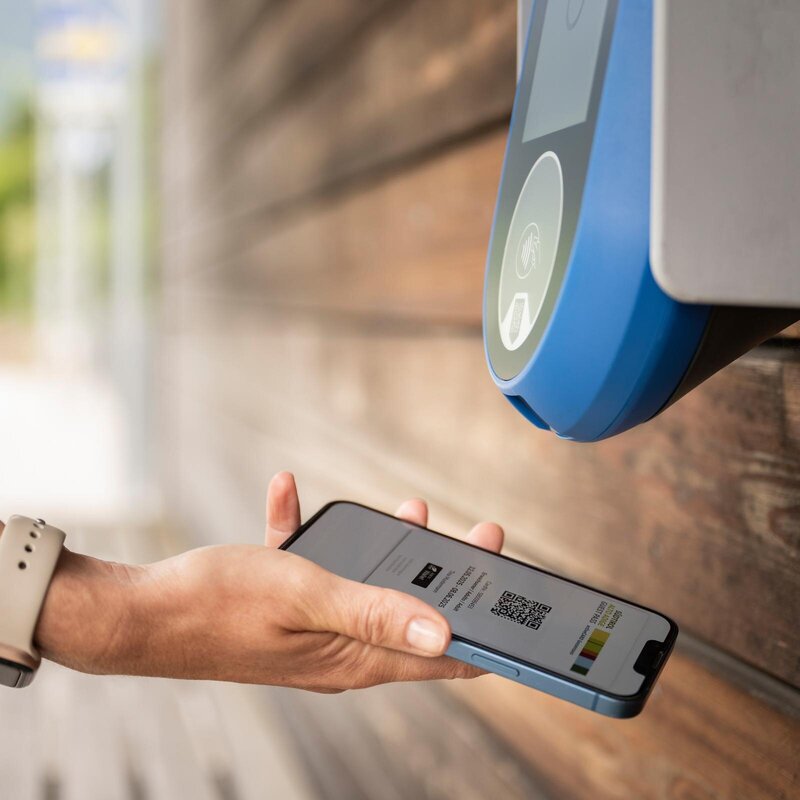 Hand hält ein Smartphone an einen Wandscanner für kontaktloses Check-in.
