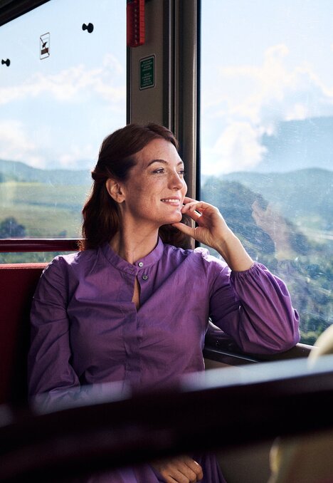 Woman sitting by the window on a train, looking out at the green mountain valley. | © IDM Südtirol-Alto Adige/Manuel Ferrigato